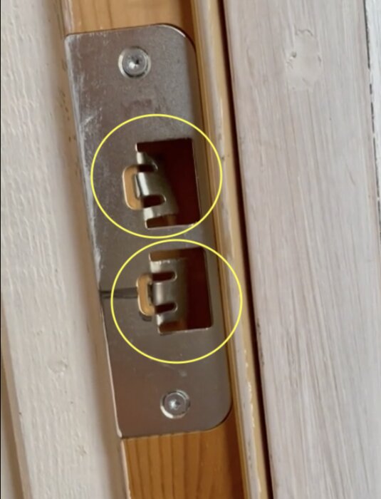 Närbild av en dörrs strikplåt med markerade flärpar för justering av dörrkolvens position.