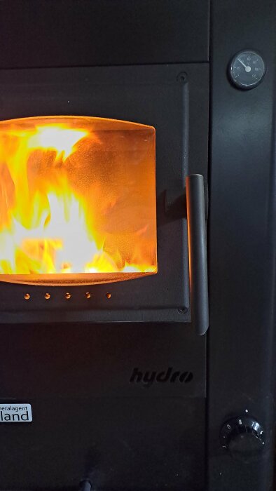 Brinnande eld i en modern köksspis med synliga lågor och temperaturmätare.