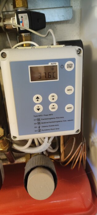 Värmesystemets styrenhet med digital display som visar en temperatur på 31,6°C, omgiven av anslutna rör och kablar.