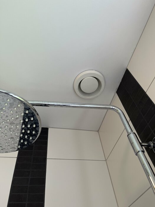 Badrumstak med enkel ventil ovanför duschhörnan med svarta kakelväggar och duschstång.