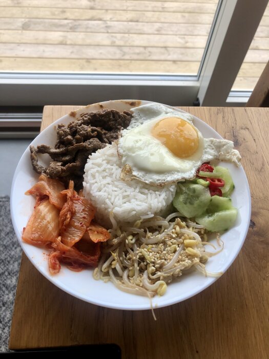 En tallrik bibimbap med ris, stekt ägg, bulgogi, kimchi, grönsaker och sesamfrön.