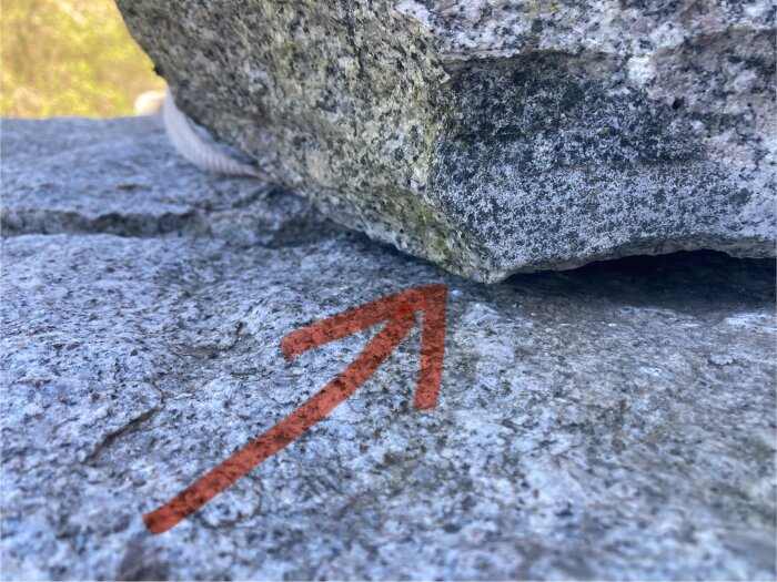 Röd pil målad på en grå stenig yta som pekar mot en stor sten.