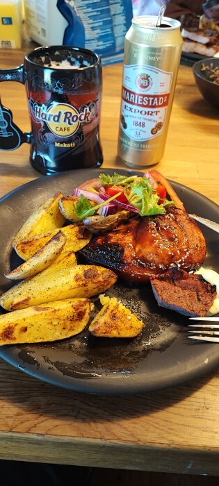 Grillad kyckling med kryddade potatisklyftor och sallad på tallrik, dryck i burk och mugg på träbord.