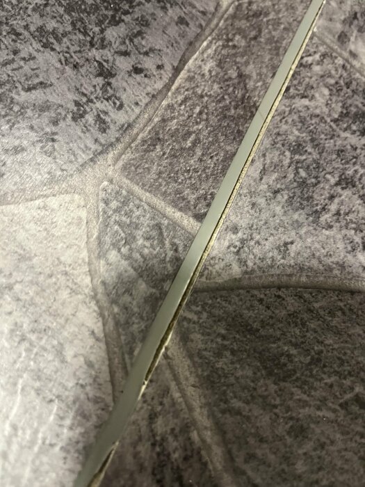 Badrumsgolv med en skarv som delvis har släppt, visande en öppning mellan två delar av golvet.