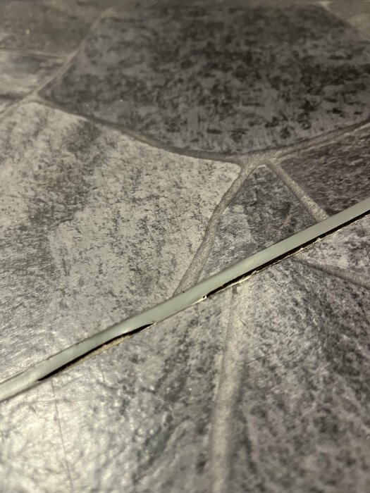 Nahaufnahme eines Badzimmerbodens mit losgelöster Fuge an einer Türschwelle, weit entfernt von der Dusche.