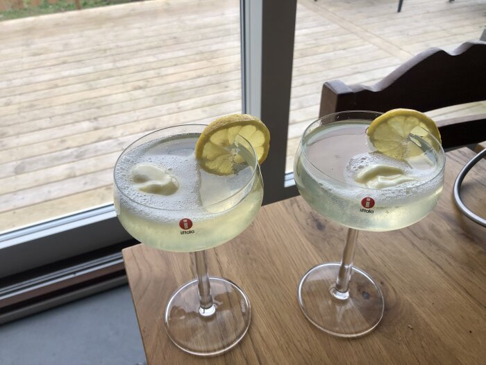 Två glas citronsorbet gin och tonic med citronskiva, på ett träbord.