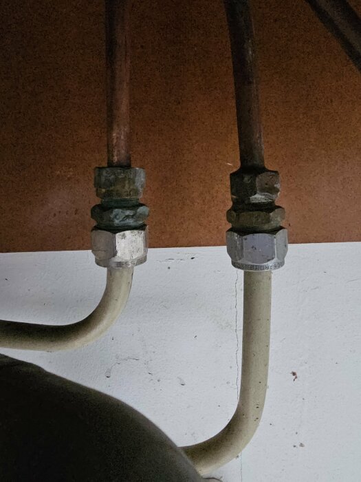 Två kopparledningar med anslutna ballofixventiler ovanför ett vitmålat avloppsrör.