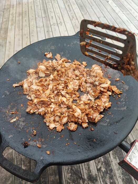 Stekt kryddad kyckling i en wokpanna med en stekspade på en träterrass.