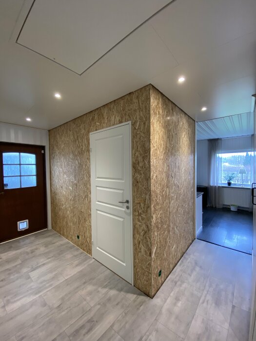 Renoveringsfas av en hallvägg med OSB-skivor och en dörr, redo för gipsning.