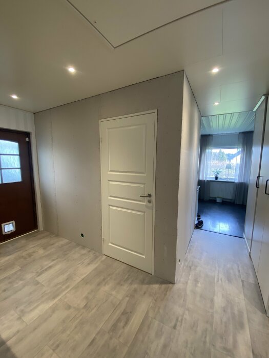 Vägg i renoveringsprocess med nya gipsplattor bredvid en vit dörr, OSB-skivor synliga, i ett hem.