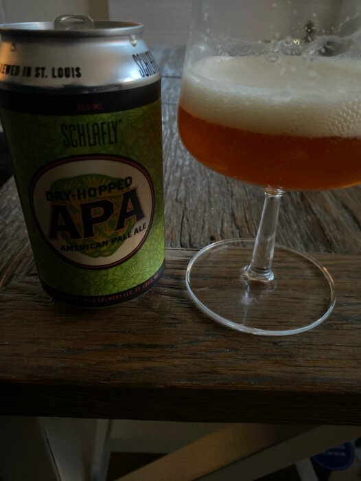Burk av Schlafly Dry Hopped APA öl och ett delvis fyllt ölglas på ett träbord.