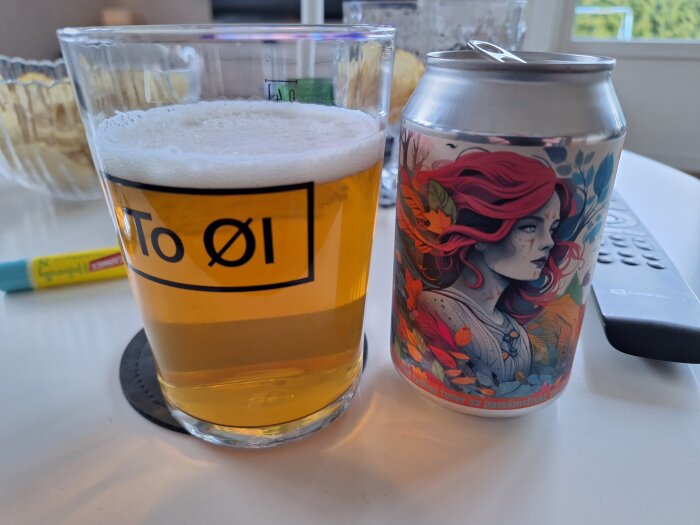 Ölglas med NIPA-öl bredvid en färgrik burk med illustration av en kvinna, på ett vitt bord.