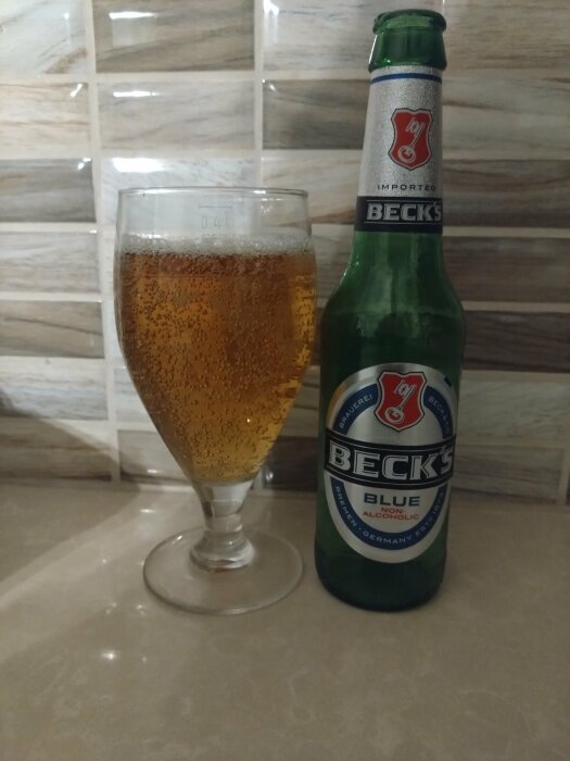 Ett glas med öl och en Beck's Blue non-alcoholic ölflaska på ett köksbord.