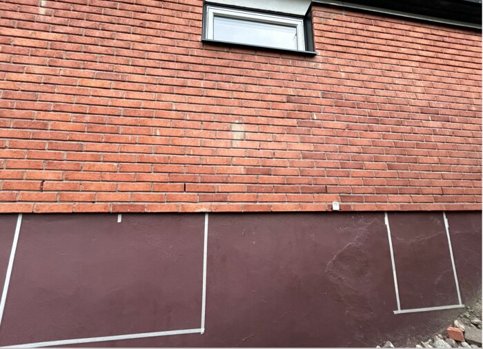 Del av husfasad med tegelsten ovanför betongvägg där ett litet fönster är inmonterat och plats för fler är markerad.