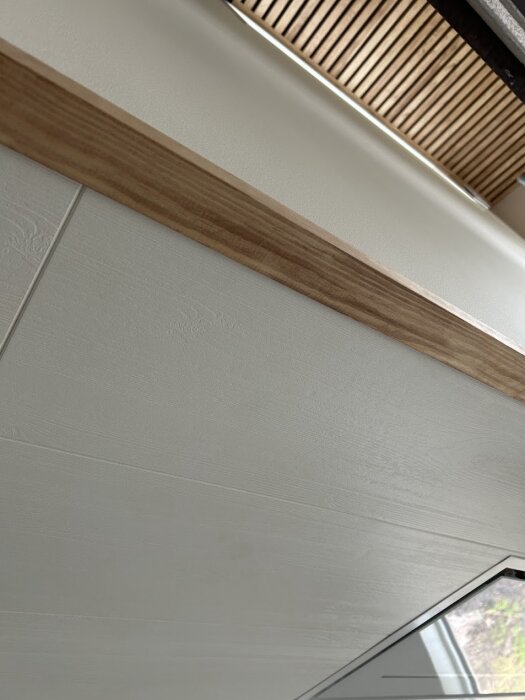 Handgjorda akustikpaneler av betsat furu ovanför en vitpräglad vägg och L-profil list som taklist.