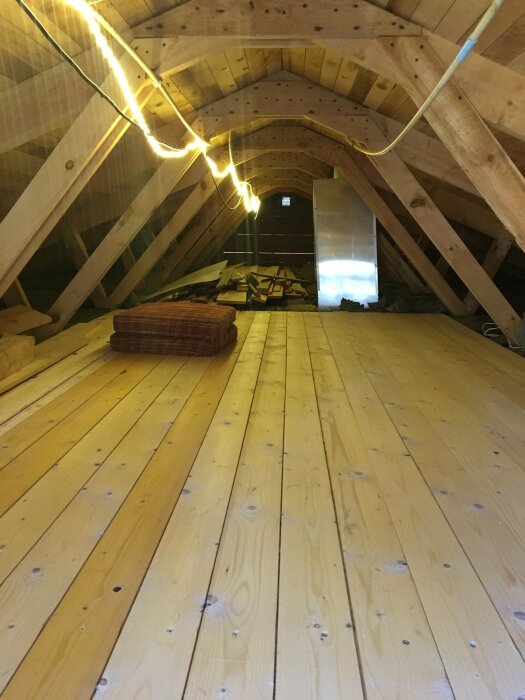 Ny lagd råspont av trä på en vind med synliga takbjälkar, byggmaterial och en ljusslinga.