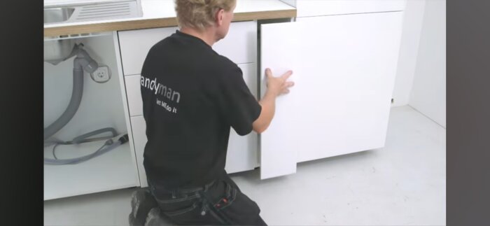 Person som monterar skåp i kök med ett eluttag placerat under diskhon.