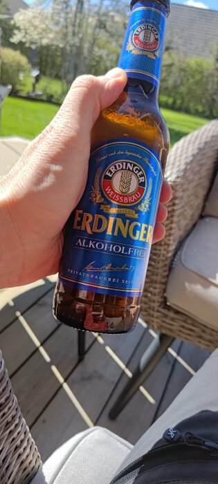 Hand håller en flaska Erdinger alkoholfri öl utomhus i solsken.