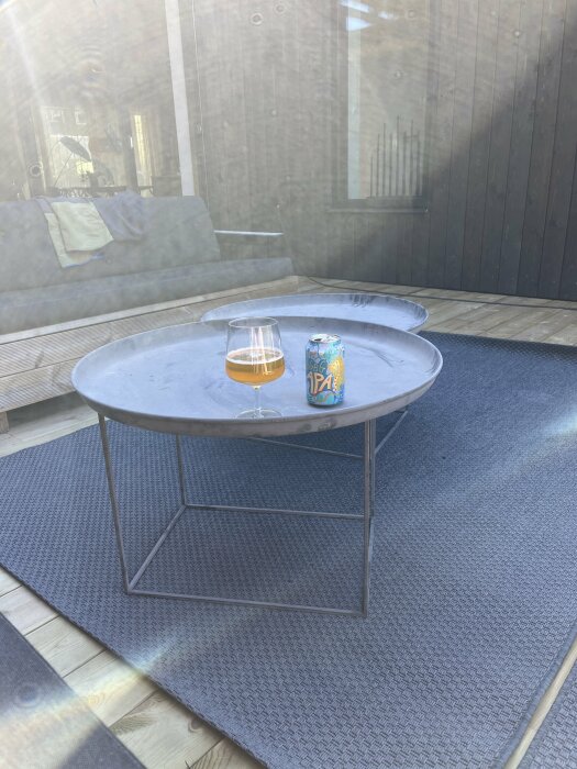 Ett glas öl och en burk på ett runt utomhusbord på en altan, viloperiod under byggprojektet.