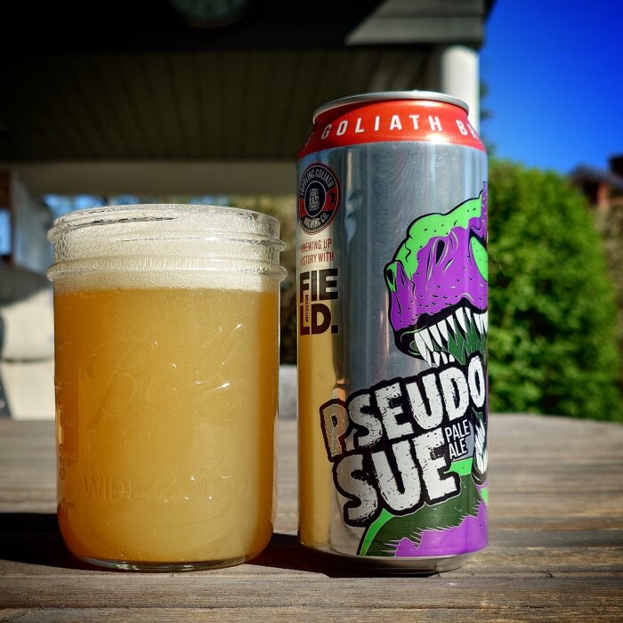 Öppnad ölburk bredvid ett glas fyllt med ljus öl utomhus i solsken.