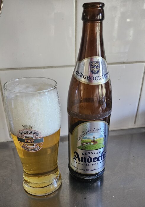 Flaska av Andechs Bergbock Hell bredvid ett glas med öl på en köksbänk.