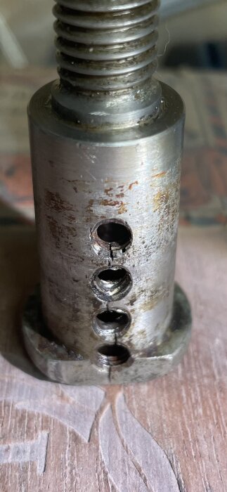 Metalldel med gängor och skador i form av sprickor runt flera hål, tecken på slitage och korrosion.