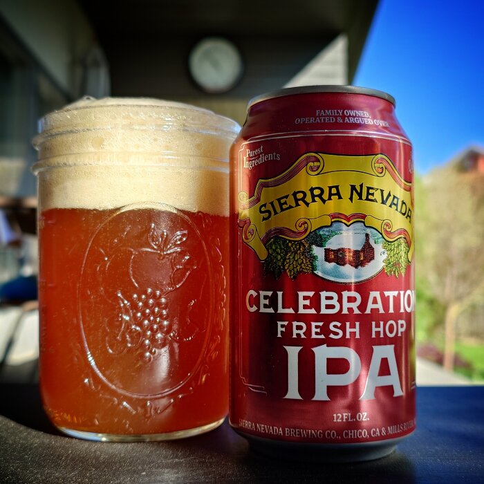 Ett glas öl och en burk Sierra Nevada Celebration Fresh Hop IPA på en bänk utomhus.