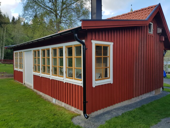 Ett nyrenoverat rött hus med vita knutar och fönster samt ett nytt tak efter lockläktsspikning.