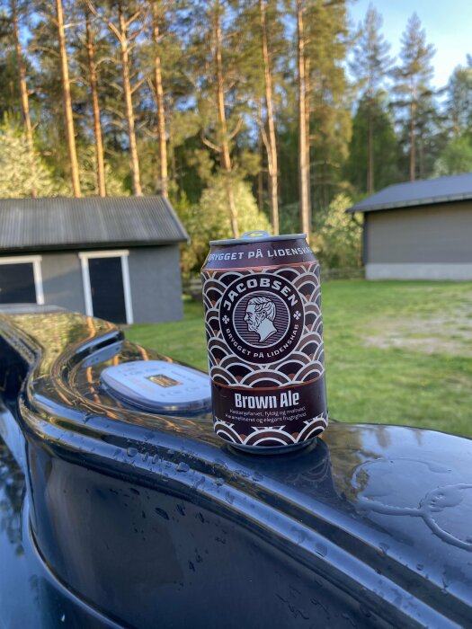 En burk Brown Ale på en glänsande svart ytterkant, trädbakgrund, uteplatsmiljö.