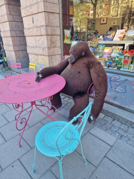 Stort brun plyschgorillabamse sitter vid ett rosa bord utanför en leksaksaffär.