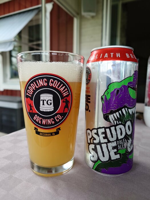 Ett glas öl bredvid en burk Pseudo Sue Pale Ale från Toppling Goliath Brewing Co. på ett bord.