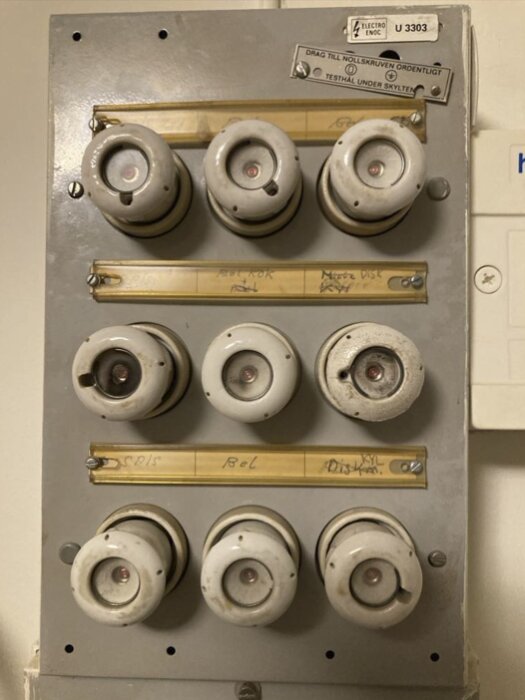 Äldre elcentral med keramiska säkringar märkta för ugn och spis.
