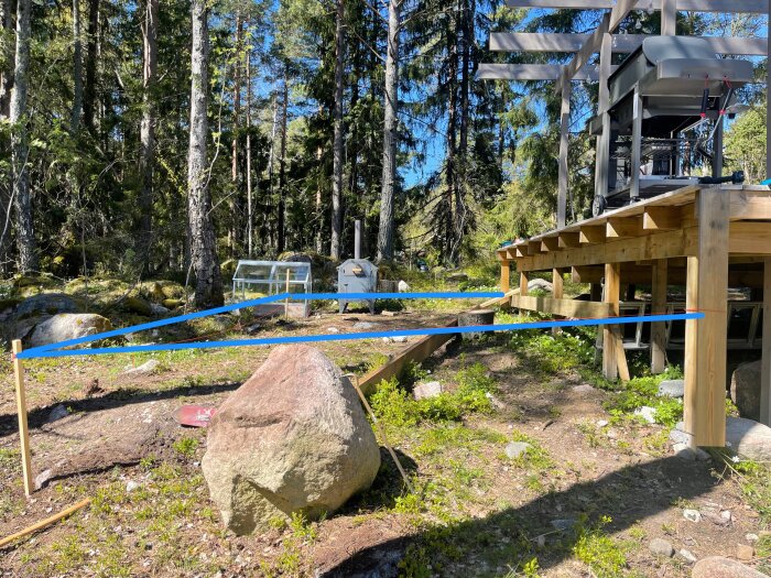 Skiss av planerad utbyggnad av altan med markerade bärlinor och stolpar mot skogsbakgrund.