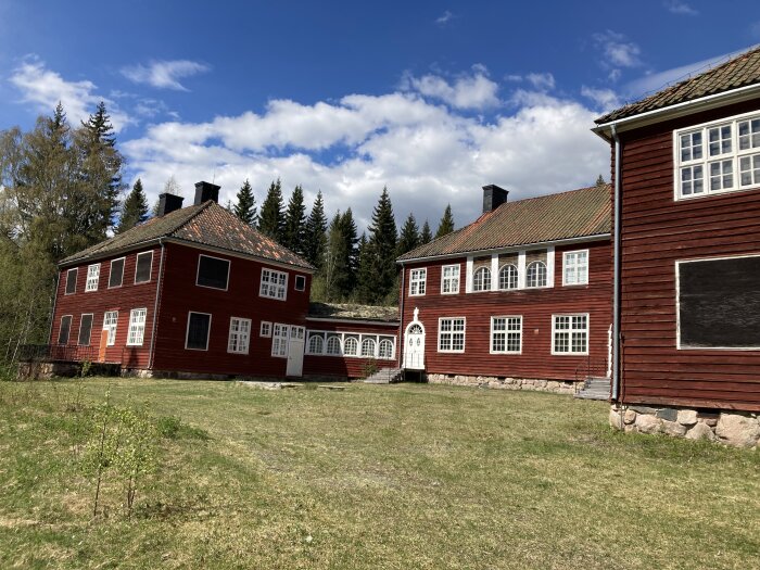 Två traditionella svenska röda trähus med vita knutar och tegeltak under solig himmel.