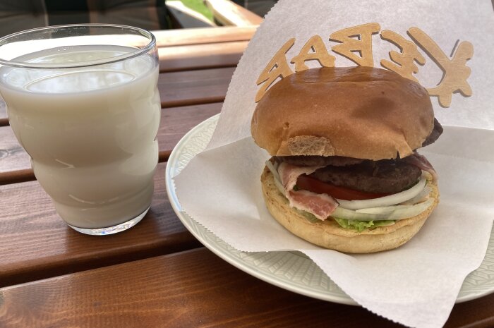 Grillad hamburgare med sallad, tomat, lök och hamburgerbröd på tallrik med ett glas mjölk på sidan.