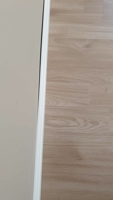 Laminatgolv bredvid en vit dörrkarm med en synlig skarv mellan golvet och karmen.