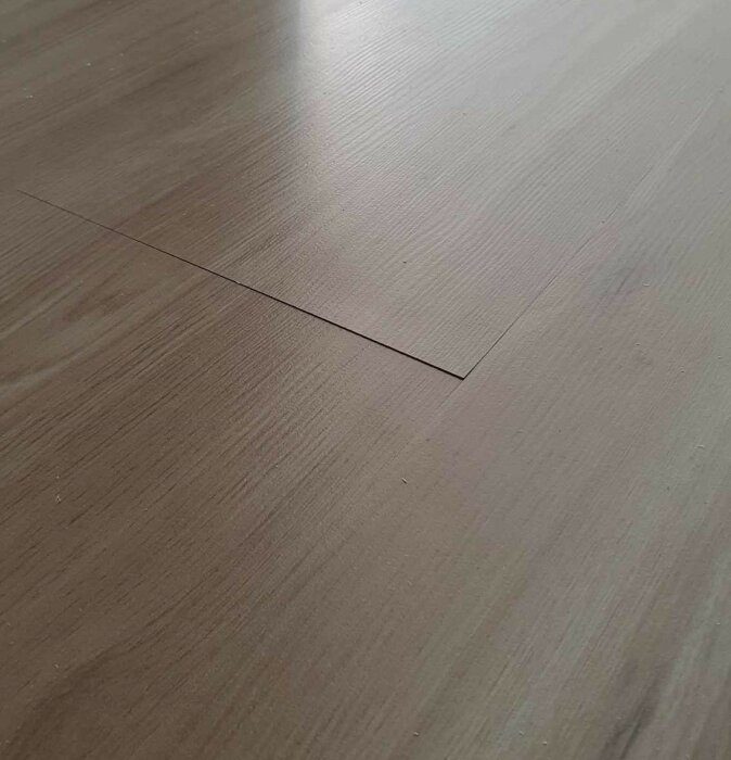 Ett golv med en synlig skarv mellan två brädor och en ojämn yta.