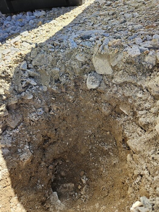 Ett grävt hål i ett lager av packat spränggrus som visar ojämn mark förberedd för altanbygge.
