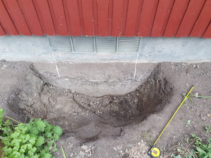 Uppmätt källarfönster och grävd grop i jord med markerade linjer på husväggen och måttband.