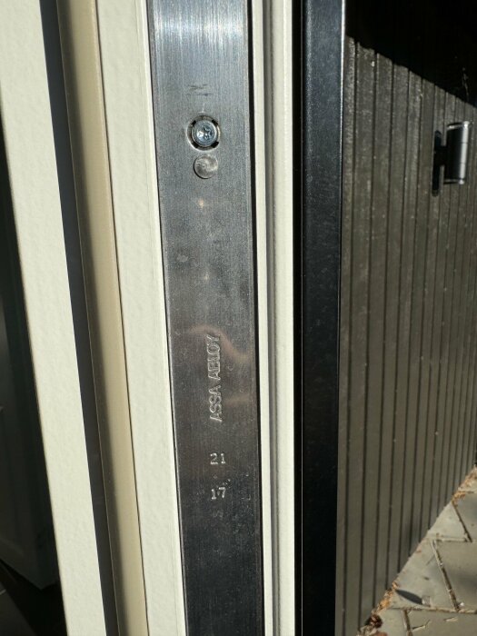 Dörrkarm med skylt som visar "ASSA ABLOY" samt skruvar, i soligt väder.