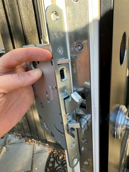 En person håller i en öppen dörr med synlig Yale-dörrlåsmekanism och låskolvar.