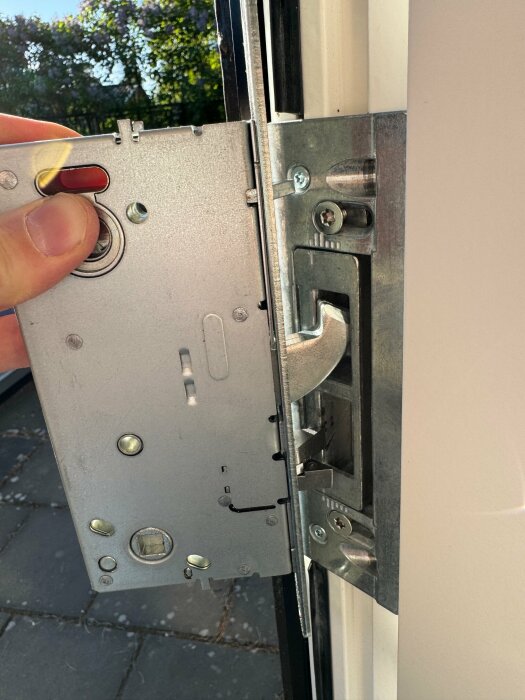 Hand håller upp en dörr med synligt dörrlås och låskista under installation eller reparation.
