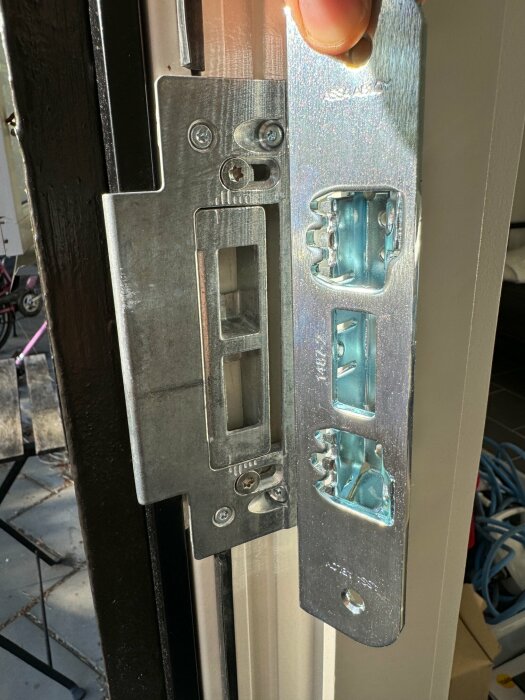 Närbild av en öppen dörrlås mekanism med synliga skruvar och metalldelar i solljus.