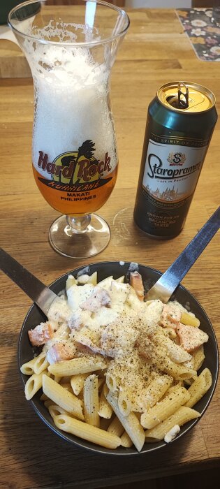 Pasta med lax och ostsås toppad med kryddor, bredvid en ölburk och ett halvtomt ölglas.