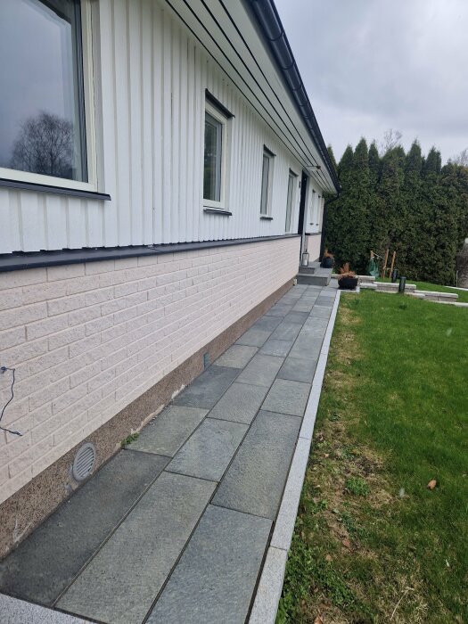 Sockel på ett hus med flagnad färg avslöjande betong, längs en grå stenlagd gångväg.