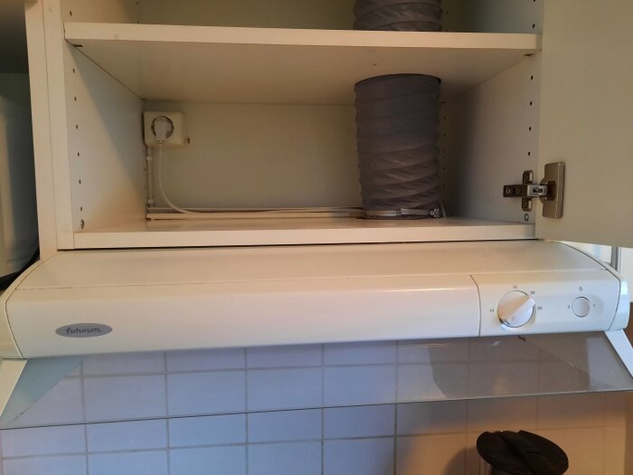 Vit fläktkåpa av märket Futurum ovanför köksspis, med tillhörande utdragbar flexibel ventilationskanal.