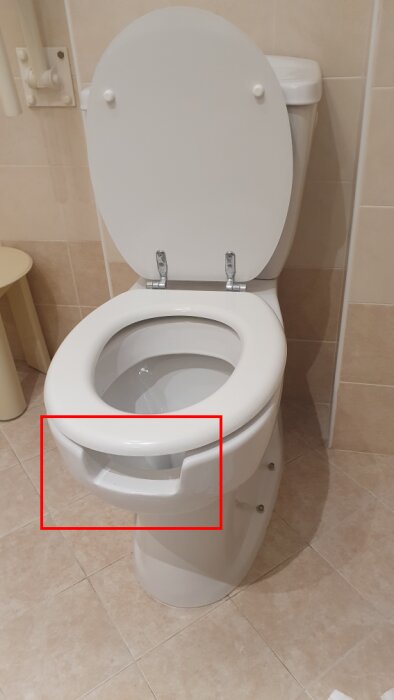 Toalett i badrum med ovanligt designat hål i framkanten av sitsen.