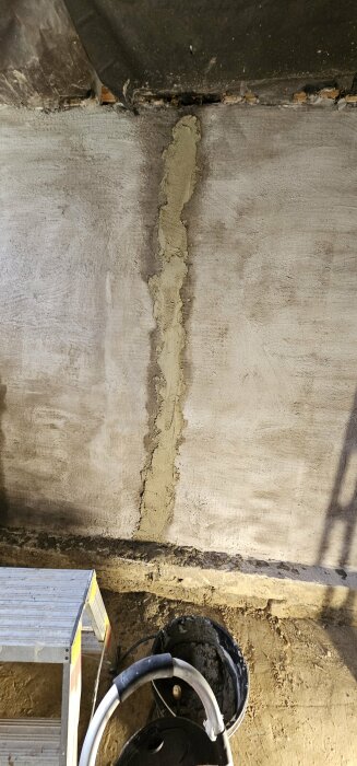 Vertikal applikation av betong på en hålsten vägg med en trälist som ramlat ner och en stege i förgrunden.