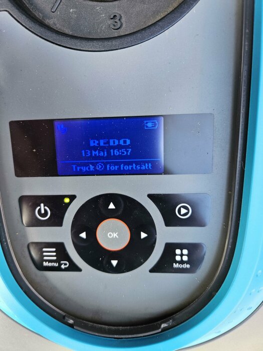 Display på en apparat med texten "REDO" och tid, omgivet av knappar inklusive en play-ikon och OK.