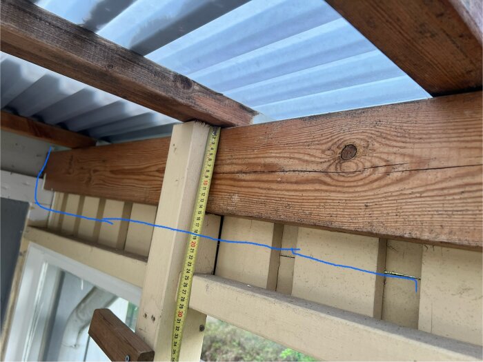 Mätning av en träregel på 145 mm med tumstock i ett underkonstruerat uterum, avsedd för renovering och installation av skjutfönster.